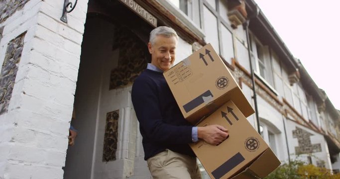 4K Cheerful mature couple moving out, carrying boxes out of their house. Slow motion.