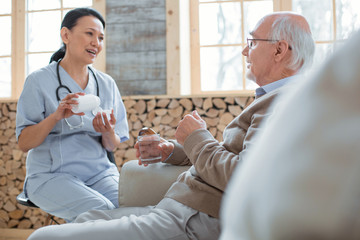 Your painkillers. Skillful optimistic doctor carrying bottle filled with pills while talking to...