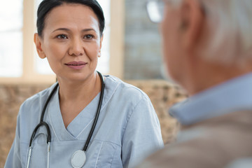 Fototapeta premium What a person. Successful positive doctor dressing in uniform while treating senior man and posing on blurred background