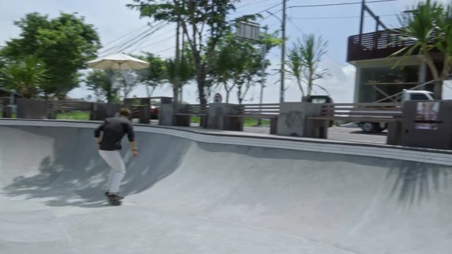 Young man riding longboard and doing trick in skatepark bowl at sunny summer day