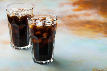 Ice coffee in a tall glass with cream poured over and coffee beans. Cold summer drink on a blue rusty background with copy space