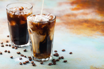 Ice coffee in a tall glass with cream poured over and coffee beans. Cold summer drink on a blue...
