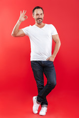 Cheerful adult man standing isolated showing okay gesture.