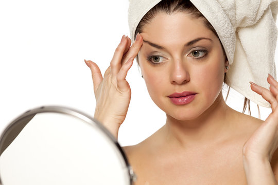 Young beautiful woman with towel on hr head on white background lifting her eyebrow with her finger