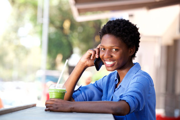 smiling young african woman sitting at cafe and making phone call