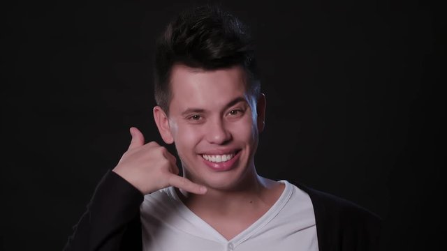A young man showing a Call me gesture against a black background. Close-up Shot