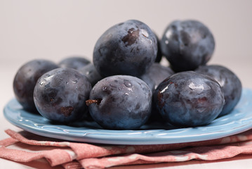 Fresh ripe blue plums on plate, wooden table with napkin