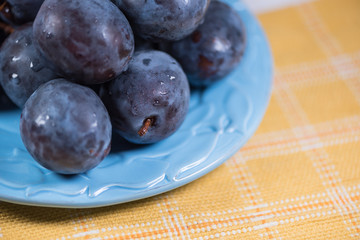 Fresh ripe blue plums on plate, wooden table with napkin