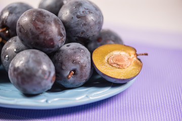 Fresh ripe blue plums on plate, wooden table with napkin