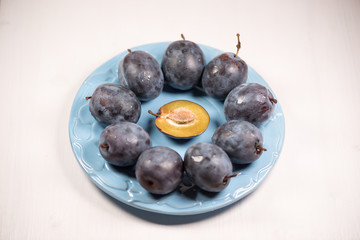 Fresh ripe blue plums on plate, wooden table