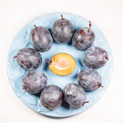 Fresh ripe blue plums on plate, wooden table