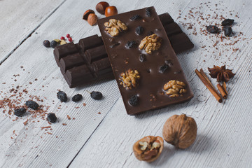 two chocolate bar filled with different berries and nuts lie old wooden table with cracked paint on the surface.scattered Almonds, nuts,buckwheat, and grated cinnamon.  strongly blurred background