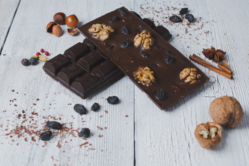 two chocolate bar filled with different berries and nuts lie old wooden table with cracked paint on the surface.scattered Almonds, nuts,buckwheat, and grated cinnamon.  strongly blurred background
