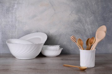 Fototapeta na wymiar A set of wooden spoons in a white bowl on a gray background on a wooden table White dishware stacked on a wooden table against grey background on wooden table