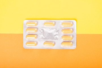 One blister of tablets on yellow and orange background.