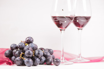 Fresh grape and red wine on the white table with two glasses, selective focus