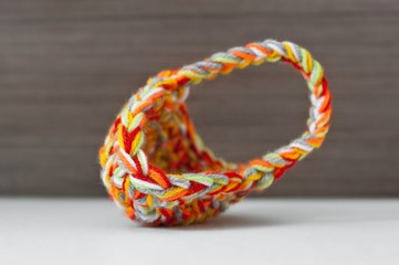 Close up crochet small colorful basket, red, yellow, orange, green, white strains on wooden texture background. Homemade decoration, crafts and arts, hobby activity. Shallow depth of focus.