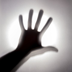 Abstract silhouette of a man's hand on the background of a bright light spot. A mystical square picture on a noisy background behind a frosted glass. Concept call for help or a terrible story.