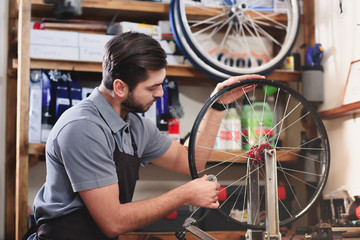 Fototapeta na wymiar young man in apron repairing bicycle wheel in workshop