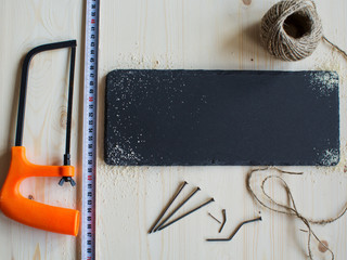 A Hacksaw, nails,roulette, ruler and sawdust on a wooden surface are ready for use.