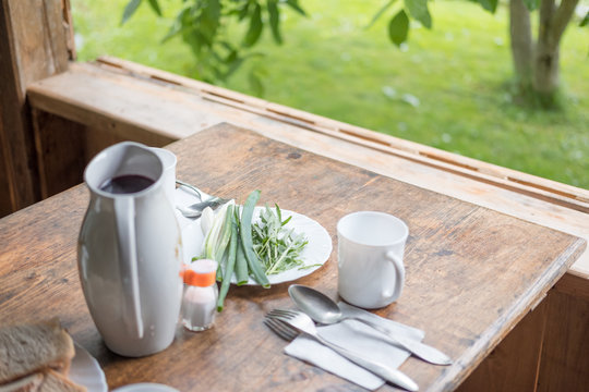 Brown mug of coffee with cinnamon and sugar on natural wooden table against defocused green tree with wooden benches.