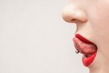 woman's mouth with red lips opened and with a piercing in a tongue 