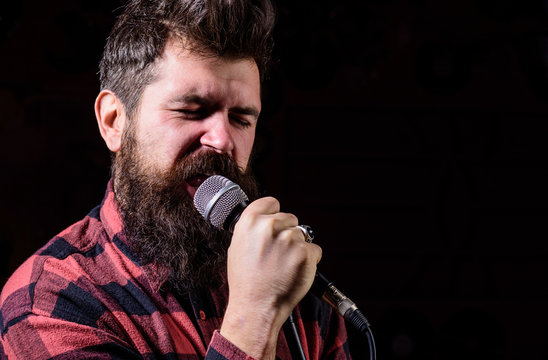 Man with tense face holds microphone, singing song, black background.