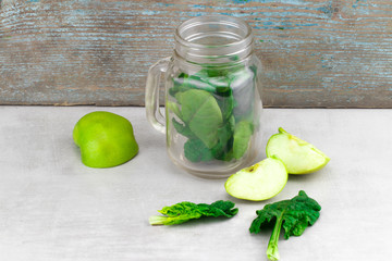Green smoothie in glass jar with fresh organic green vegetables and fruits on grey background. Spring diet, healthy raw vegetarian, vegan concept, detox breakfast, alkaline clean eating. Copy space