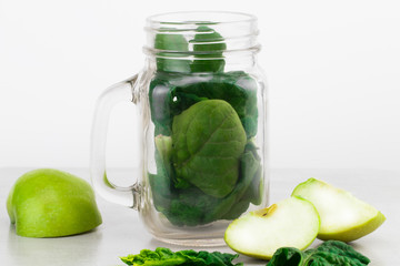 Green smoothie in glass jar with fresh organic green vegetables and fruits on grey background. Spring diet, healthy raw vegetarian, vegan concept, detox breakfast, alkaline clean eating. Copy space