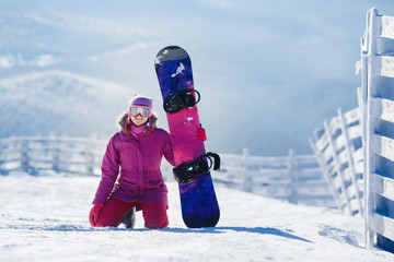 Snowboarding. Young woman sits on snow and holds snowboard. Copyspace