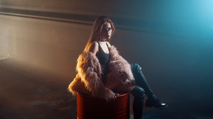 Young seductive woman, portrait in darkness. Girl in stylish pink fur coat and glasses