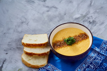 Porcelain bowl of pumpkin soup on napkin over white textured background, close-up, selective focus, top view.
