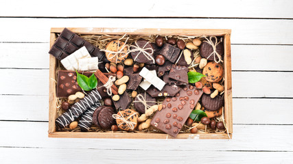 A set of milk chocolate and black chocolate in a wooden box with nuts and biscuits. On a white wooden background. Copy space for text.