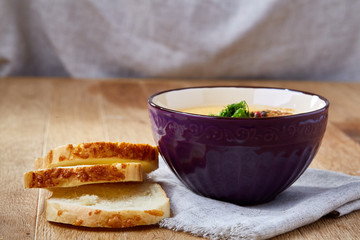 Ceramic bowl of pumpkin soup on napkin over rustic wooden background, close-up, selective focus, top view.