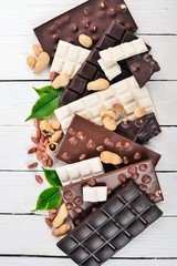 Assortment of chocolate with nuts, cookies and cocoa. On a white wooden background. Top view. Copy space for text.