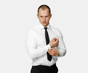 businessman a white shirt black tie, corrects cuff links on a shirt, on gray background