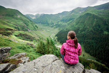 Naklejka na ściany i meble Horizontal rear view shot of a female traveller enjoying stunning mountains scenery sitting on the edge of a rock copyspace travelling trip extreme hiking lifestyle ecology environmental peace.