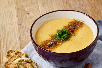 Ceramic bowl of pumpkin soup on napkin over rustic wooden background, close-up, selective focus, top view.