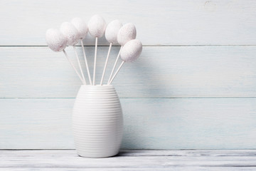 White decorative eggs in vase over wooden background.