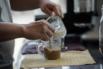 Hand of male barista holding and pouring milk for cup of coffee in the workplace at cafe