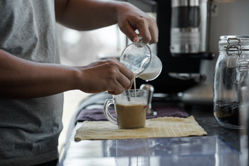 Fototapeta na wymiar Hand of male barista holding and pouring milk for cup of coffee in the workplace at cafe