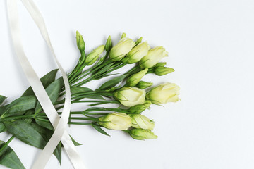 Obraz premium White eustoma fresh flowers on light white background with copy space. Floral greeting card with rose buds. Top view.
