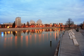 Budynki mieszkalne i most Grunwaldzki nad rzeką Odrą we Wrocławiu wieczorem.