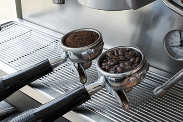 An two espresso handle filled with ground coffee and seed located at the coffee machine at cafe.