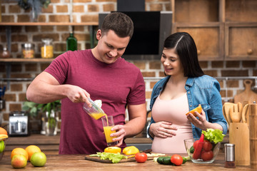 happy young pregnant couple squeezing fresh juice together