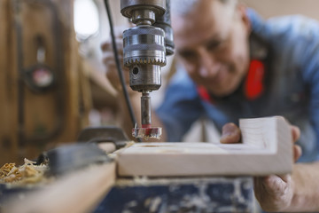 Mature carpenter using drill press in workshop