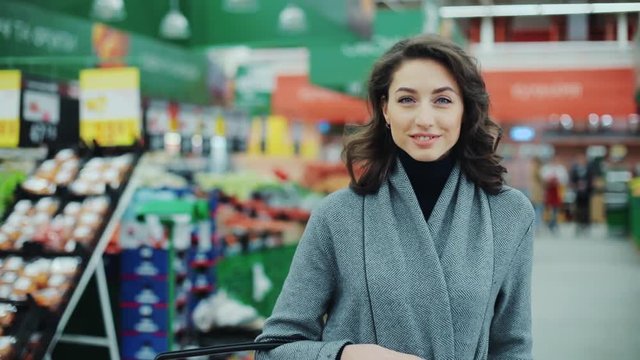 Portrait young woman stands look at camera and smiles while in a produce section in supermarket feel happy girl shopping face retail store pretty customer happiness casual market food consumer