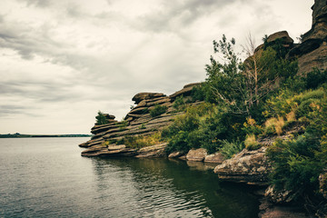 Fototapeta na wymiar Rocky shore on lake in cloudy weather. Stones of unusual shape.