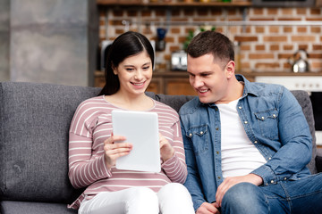 Fototapeta premium smiling young pregnant couple using digital tablet together at home