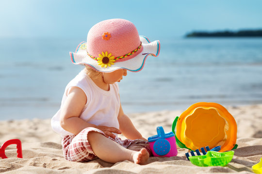 one year old girl sitting at the sea with bucket. Child outdoors at the beach in summer